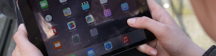 Zwei Hände halten ein iPad, auf dessen Bildschirm verschiedene App-Symbole zu sehen sind.